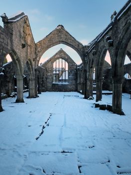 the medieval ruined church in heptonstall covered in snow showing arches and columns against a blue winter sky