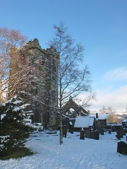 a scenic view of the medieval ruined church in the village of heptonstall west yorkshire covered in snow with surrounding graves trees and houses
