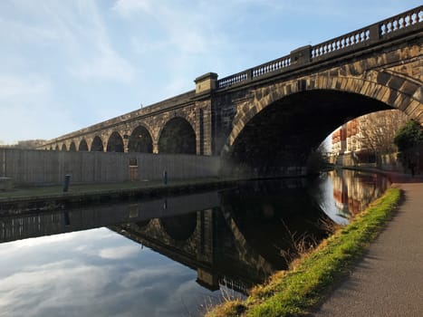 Old abandoned railway viaduct crossing the canal in leeds city centre near whitehall road with arched reflected in the water