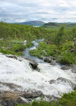 Streamlet waterfall from Lake Tsahkal in Northern Lapland wilderness, fells on the background