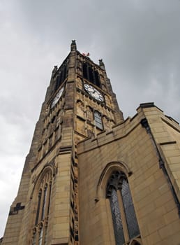 view of the clock tower and building of the historic saint peters parish church in the center of huddersfield against a cloudy sky