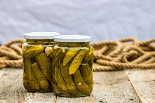 Glass jars with pickled red bell peppers and pickled cucumbers (pickles) isolated. Jars with variety of pickled vegetables. Preserved food concept in a rustic composition.