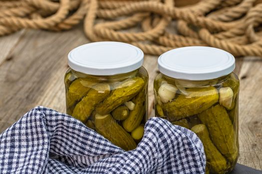 Glass jars with pickled red bell peppers and pickled cucumbers (pickles) isolated. Jars with variety of pickled vegetables. Preserved food concept in a rustic composition.