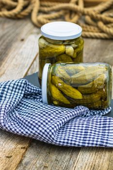 Glass jars with pickled red bell peppers and pickled cucumbers (pickles) isolated. Jars with variety of pickled vegetables. Preserved food concept in a rustic composition.