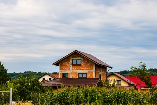 Development area at the edge of the village, facade of new unfinished house. Green corn field in front of house.