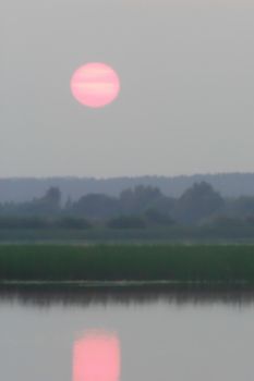 pink sunset in the haze over the lake and forest, blurred photo