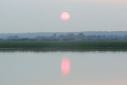 pink sunset in the haze over the lake and forest, blurred photo