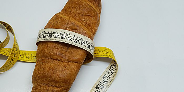 soft measuring ruler wrapped around a croissant as a symbol of unhealthy nutrition, copy space