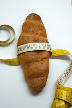 soft measuring ruler wrapped around a croissant as a symbol of unhealthy nutrition, on a white background
