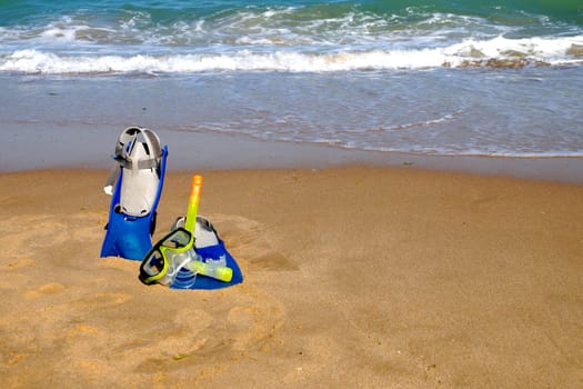 flippers and mask for swimming on the sand against the background of the sea and clear sky, copy space