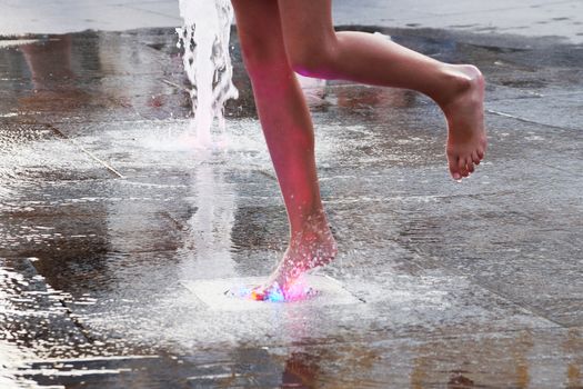 a girl touches a fountain on the sidewalk with her bare foot