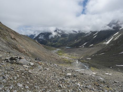 Summer view of alpine mountain valley with winding stream and glacial lake, Sulzenauferner Glacier, Stubai Alps, Austria.
