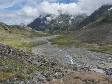 Summer view of alpine mountain valley with winding stream and glacial lake, Sulzenauferner Glacier, Stubai Alps, Austria.