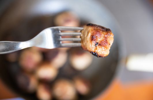 In the blurred background of a kitchen a close-up image of a meatball skewered by a fork.