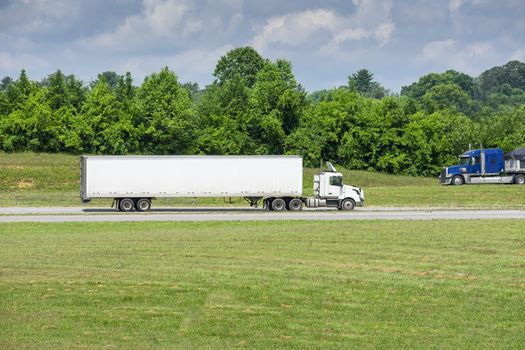 Two heavy trucks meet on a summer morning. Heat waves from the pavement create an interesting slight shimmer on the trucks and background foliage.