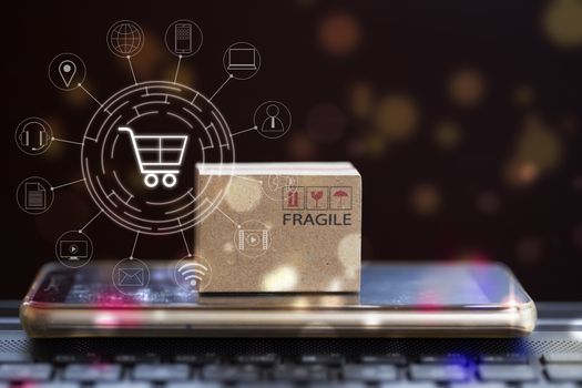 Online shopping, e-commerce concept: Cardboard box with smartphone on notebook keyboard and icon customer network connection. Product service and delivery to consumers by connecting with the internet.