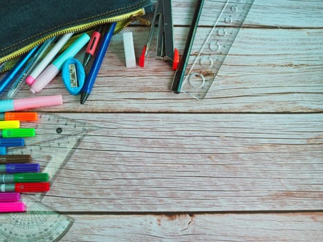 The top view of  stationery in school bags and pencils arranged on a wood teble background.