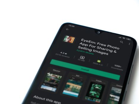 Lod, Israel - July 8, 2020: EyeEm - Sharing & Selling Images app play store page on the display of a black mobile smartphone isolated on white background. Top view flat lay with copy space.
