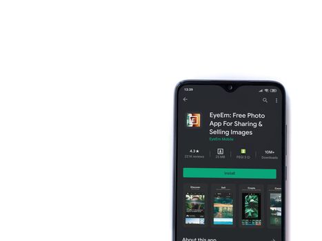 Lod, Israel - July 8, 2020: EyeEm - Sharing & Selling Images app play store page on the display of a black mobile smartphone isolated on white background. Top view flat lay with copy space.