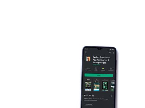 Lod, Israel - July 8, 2020: EyeEm - Sharing & Selling Images app play store page on the display of a black mobile smartphone isolated on white background. Top view flat lay with copy space.