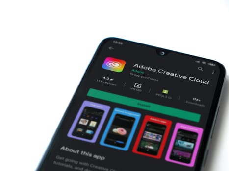 Lod, Israel - July 8, 2020: Adobe Creative Cloud app play store page on the display of a black mobile smartphone isolated on white background. Top view flat lay with copy space.