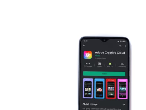 Lod, Israel - July 8, 2020: Adobe Creative Cloud app play store page on the display of a black mobile smartphone isolated on white background. Top view flat lay with copy space.