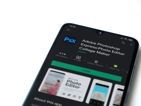 Lod, Israel - July 8, 2020: Adobe Photoshop Express Photo Editor app play store page on the display of a black mobile smartphone isolated on white background. Top view flat lay with copy space.