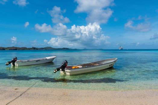 Fiji, South Pacific -- February 7, 2016. Two motorboats are anchored on a Fiji beach; a cruise ship is on the horizon.