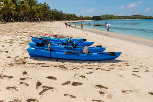 Fiji, South Pacific -- February 7, 2016. Bright blue paddle boats lie on a Fijian beach being visited by tourists.