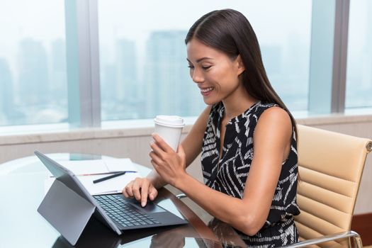 Portrait of a happy startup Asian woman businesswoman working on laptop or shopping online at home office while drinking a coffee cup.