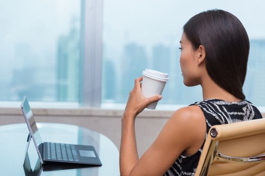 Businesswoman taking a coffee break at work looking out the window thinking about career opportunities or life goals. Asian business woman drinking hot drink in office.