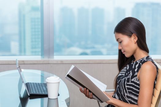 Asian chinese businesswoman reading documents studying paperwork at desk. Businesswoman, lawyer or accountant doing contract work in city office in Shanghai, China.