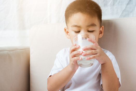 Close up of happy Asian little cute child boy hand holding milk glass he drinking white milk during sitting on the sofa at home after lunch. Daily life health care Medicine food