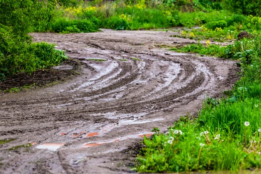 dirty clay mud road zig-zag turn with puddles and tire tracks - closeup with selective focus and blur