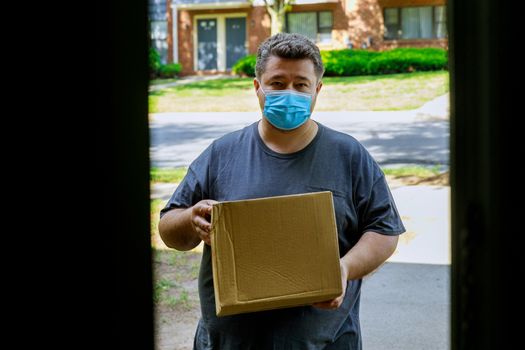 Delivery man wearing face mask giving a cardboard box at the entrance of home delivery during the quarantine of the coronavirus pandemic.