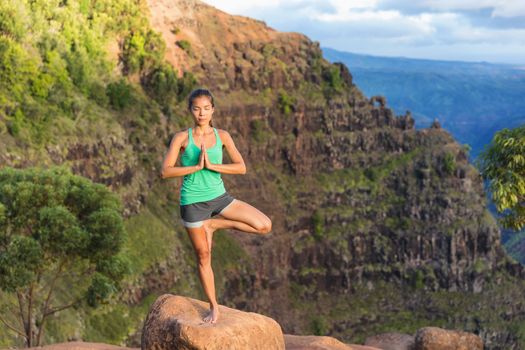 Yoga meditation - woman meditating doing yoga tree pose on Kauai, Hawaii, USA. Serene relaxing girl in amazing nature landscape in Waimea Canyon.