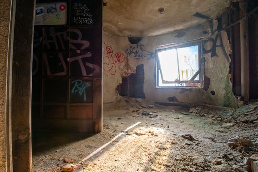 A Small Room in an Abandoned Building With Light Coming Through a Window and a Large Metal Door Covered in Graffiti