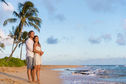 Relaxing casual couple watching sunset together on Waiohai beach, Poipu in Kauai, Hawaii. Beautiful nature landscape for copyspace.