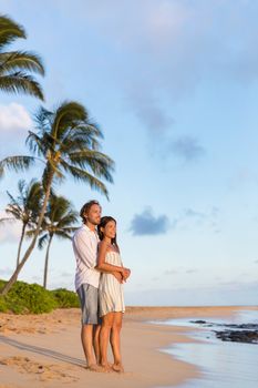 Relaxing couple watching sunset on beach vacation. multiracial people enjoying tropical holidays together hugging in love.