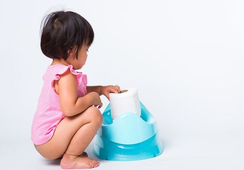 Asian little cute baby child girl education training to sitting on blue chamber pot or potty with toilet paper rolls, studio shot isolated on white background, wc toilet concept