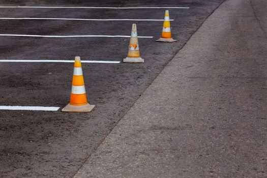 Orange road cones on a asphelt driving area with white lines, close-up with selective focus and backgropund blur.