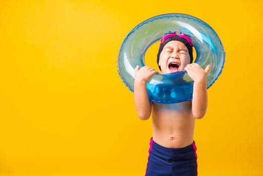 Summer vacation concept, Portrait Asian happy cute little child boy wear goggles and swimsuit hold blue inflatable ring, Kid having fun on summer vacation, studio shot isolated yellow background