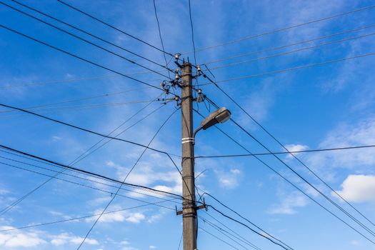 Concrete lamp post with many cables connected radially on blue sky with feather clouds in the background, Centered composition. Old electrical grid theme,