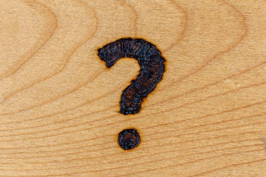 question mark drawn with handheld woodburner on bright flat wooden surface.