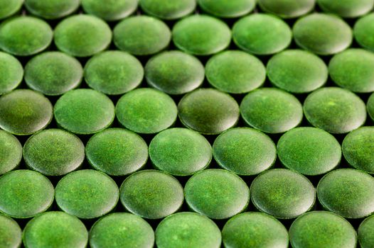 close-up background of many green organic spirulina tablets laid tight in one layer on flat surface.