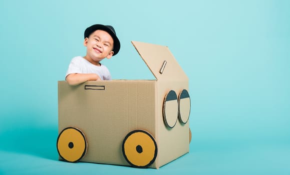 Happy Asian children boy smile in driving play car creative by a cardboard box imagination, summer holiday travel concept, studio shot on blue background with copy space for text