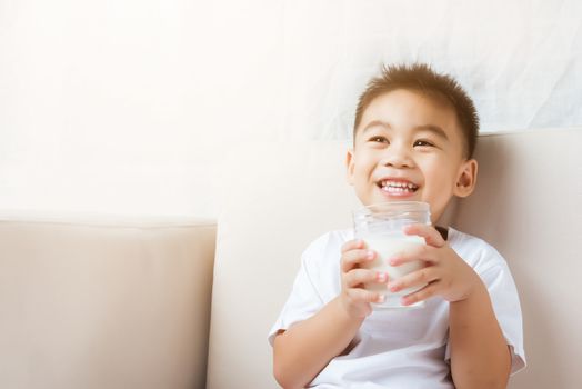 Close up of happy Asian little cute child boy hand holding milk glass he drinking white milk during sitting on the sofa at home after lunch. Daily life health care Medicine food