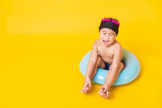 Summer vacation concept, Portrait Asian happy cute little child boy wear goggles, swimsuit hold beach blue inflatable ring, Kid have fun sit in inflatable, studio shot isolated yellow background