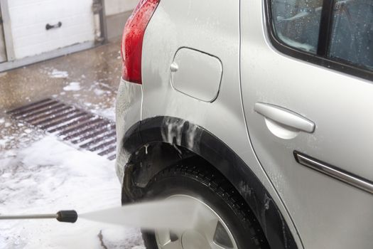 a process of indoor small silver car washing with stream of water from hose by hand