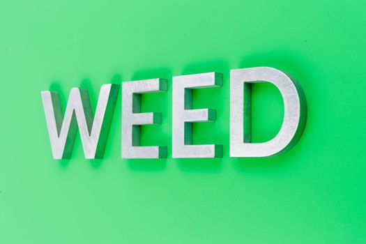 the word weed laid with silver metal letters on pastel green background with linear perspective and selective focus